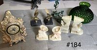 Clock, eagle bookends, alabaster/marble figurine bookends, chess knight bookends, green glass lamp shade, metal candle holders, home security device, and matchbooks visible on table