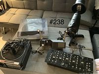 Photo of all items on a tufted sofa, including turntable, projector, lighting unit, and DJ mixer