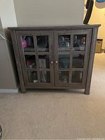 Front view of wooden 2 level cabinet with glass paneled double doors showing the dark wood finish and interior shelves.