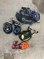 Photo shows all items laid out on concrete floor including bike helmets, gloves, backpacks, repelling harness, carabiners, and rope.
