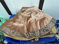 Gold Christmas tree skirt with sequined trim on blue chair, showing velvety texture and shiny border.