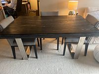 Photo of a dark black and white marbled rectangular dining table with angled white legs, chairs around, scratches visible.