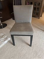 Front view of one light gray upholstered dining chair showing seat, backrest, legs, and silver nailhead trim