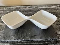 White ceramic double dip dish with two square compartments and rounded edges on a dark surface.
