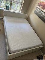 White Ikea double bed frame with Endy double mattress in a corner bedroom setup near window and wall with artwork.