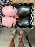 Top view photo showing two pairs of boxing gloves, pink and black, placed in a woven basket with orange hand wraps and jump rope inside.