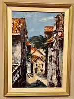Front view of framed textured painting showing an Italian medieval village with stone buildings, rust roofs and palm tree.