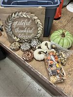 Photo showing wooden sign, three metallic pumpkin decorations, green pumpkin, three white pumpkins, and multiple bags of potpourri arranged on the floor.