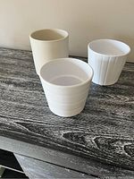 Three white vases with different shapes and textures, placed on a wooden surface