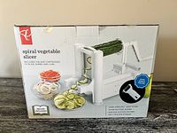 Photo of the box with image and details of the spiral vegetable slicer showing its features including three blade cartridges and a bonus peeler, suction cup feet for stability, hand operation, and included recipe ideas.