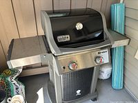 Front view of Weber Spirit gas grill showing black lid with thermometer, side shelves, and base with logo.