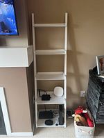 Photo of the white five-level standing shelf against beige wall showing items placed on shelves and condition of the shelf.