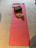 Photo of a pink Lululemon yoga mat laid flat on carpet with two green speckled yoga blocks stacked and a white yoga strap coiled on top.