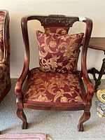 Front view of wooden armchair with floral-patterned burgundy and gold upholstery and matching cushion