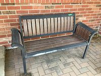 Front angle view of wooden slat and metal trim bench against brick wall, showing weathering and wear.