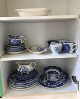 Shelved set of blue and white dishware including teacups, saucers, bowls, dinner plates, and creamer with floral and geometric patterns