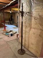 Full view of the vintage metal coat tree showing the four hooks and decorative base against the basement wall.