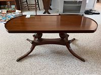 Full front view of Mersman wooden coffee table showing rectangular top and pedestal base with metal feet.