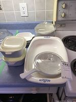 Display of Corning Ware dishes including the baking tray, shallow pan with glass lid, and two casserole dishes with plastic lids.