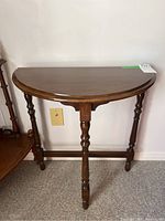 Front view of a wooden demilune table showing semi-circular top and three turned legs