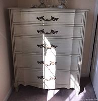 Front view of cream painted serpentine chest showing five drawers and ornate metal pulls
