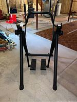 Front view of black glider exercise machine showing foot pedals, central frame, and push handles.