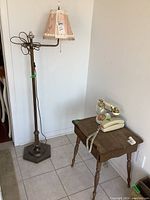 Full view of brass floor lamp with pink shade and two vintage phones on small wooden table
