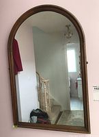 Front view of the wood framed arched mirror mounted on a wall near staircase and hallway.