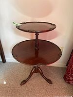Front view of two tier wooden table showing carved scalloped edges and central support.