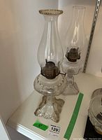 Two glass oil lamps displayed side by side. The tallest lamp is approx 18 inches with scalloped base.