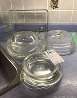 Overview of various Pyrex and Anchor Hocking glass bakeware items including rectangular and round casserole dishes, pie plates, and several glass lids on a kitchen counter.