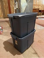 Two stacked Rubbermaid Roughneck storage totes with lids in a basement setting.