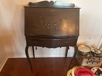 Front view of the wood secretary cabinet showing drop front closed and drawer below with decorative curved legs and top molding.