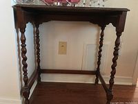 Wood side table with twisted spindle legs shown against a wall with an outlet visible behind it.