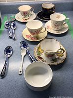 Lot contents including six tea cups with matching saucers, one white Wedgwood bowl, and seven ceramic spoons with blue floral Gzhel patterns on a countertop.
