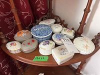 Full view of 11 assorted small trinket boxes on wooden shelf, various shapes and floral decorations