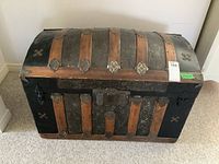 Front view of wood trunk showing wood and metal construction, with decorative metal lock plate and leather-like covering