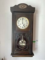 Front view of the wall clock with closed door showing carved wooden details and clock face.