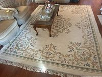 Full view of sculpted wool rug with floral and scroll motifs under wooden coffee table on hardwood floor.