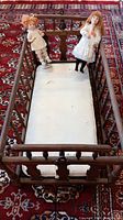 Top view of antique wooden doll cradle with two vintage dolls inside resting on white padding