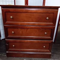 Front view of the dresser showing all three drawers with brass knobs, minor scratches on the wood surface.