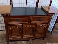 Buffet sideboard cabinet with top lifted open revealing extended longer surface top and exposed black inner surface.