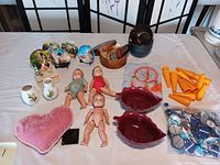 Overview of the lot showing dolls, butter pat plates, wood bowls, vases, yellow cones, and pins arranged on a table.