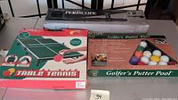 Photo shows boxed Outman Periscope, red and green Table Tennis portable set box, and Golfer's Putter Pool boxed game with golf ball style pool balls.