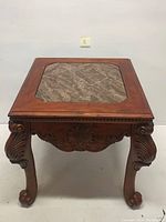 Front view of square wooden center table with octagonal marble inset top, carved apron and cabriole legs.