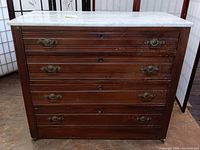 Front view of antique wooden dresser showing four drawers with ornate metal handles and scratches on finish.