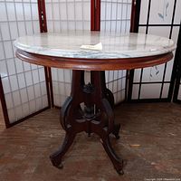 Front side view of vintage round marble top wooden table on caster wheels, showing wooden pedestal base and marble top.