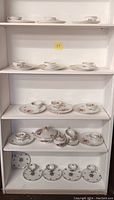 Multiple shelves showing various teacup sets and serving pieces arranged with visible floral patterns in porcelain china.