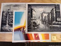Three oil paintings on canvas, showing abstract coloring in one, lighthouse seascape in black and white in the second, and Venice canal seaside grayscale in the third.