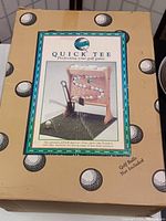 Boxed golf practice set named Quick Tee showing product image and branding, designed to improve golf game with automatic ball dispenser.